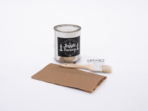 The Joggle Factory Charleston Green paint, with a piece of sandpaper, paint brush and The Joggle Factory sticker on white background.