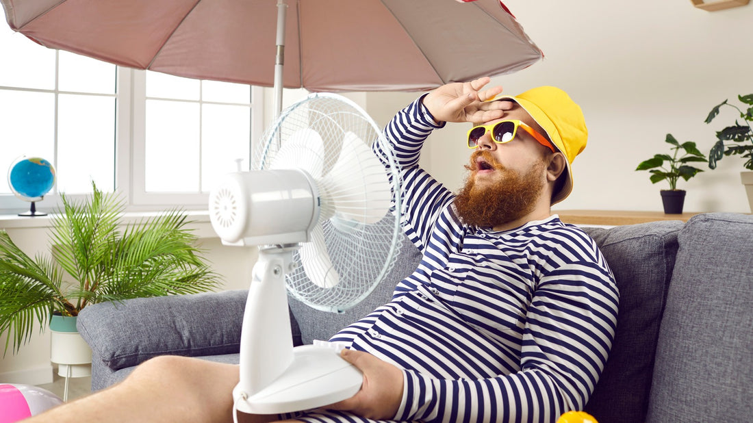 Heavy set guy with yellow hat running a fan on himself to cool off from the dreaded Summer heat.