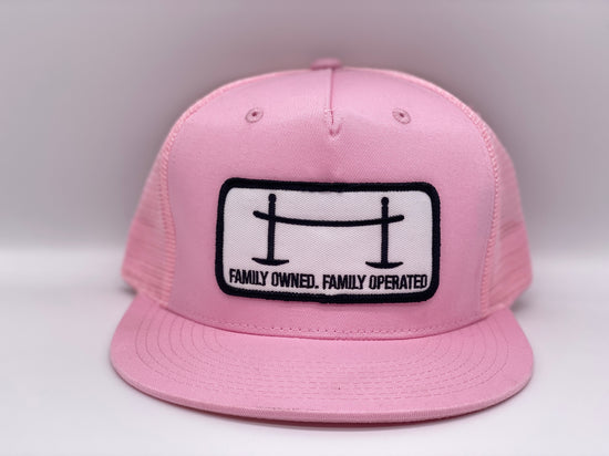 Front view of The Joggle Factory pink trucker hat with patch reading Family Owned Family Operated.
