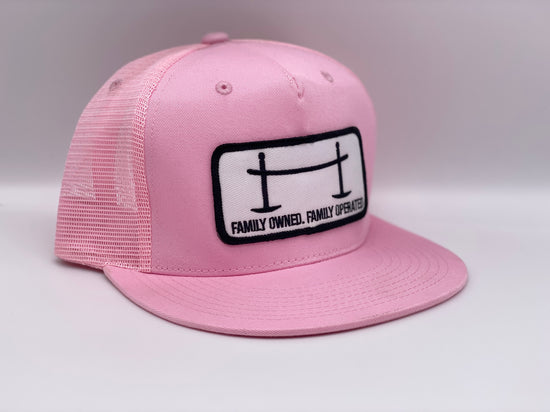 Side view of The Joggle Factory pink trucker hat with patch reading Family Owned Family Operated.